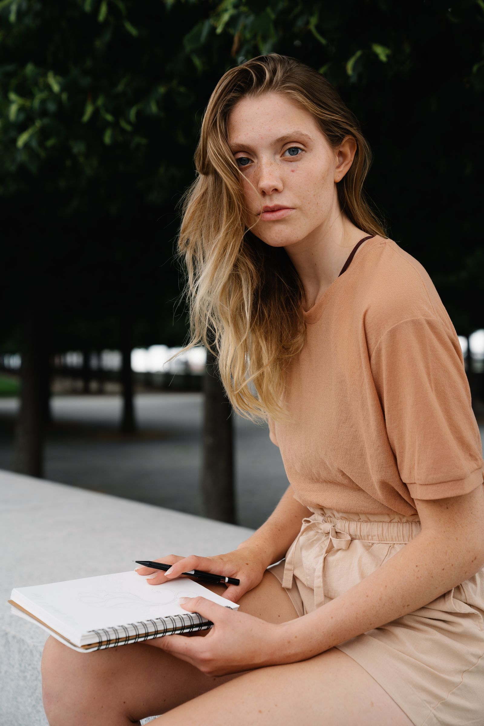 A woman sitting outdoors with a notebook and pen